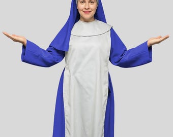 May include: A full-length image of a person wearing a blue and white nun costume. The costume includes a blue dress, a white apron, and a blue head covering. The person is smiling and has their arms outstretched.