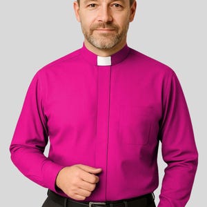 May include: A magenta clerical shirt with a white collar. The long-sleeved shirt has a pocket on the left side and is buttoned at the cuffs. The person is wearing a black belt and dark grey trousers.