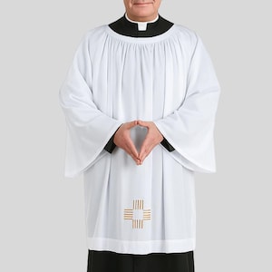 Op de afbeelding: Een witte liturgische albe met een gouden kruisontwerp op de voorkant. De albe heeft lange, wijde mouwen en wordt over een zwarte soutane gedragen. De persoon draagt een zwarte kraag en een witte priesterboord.