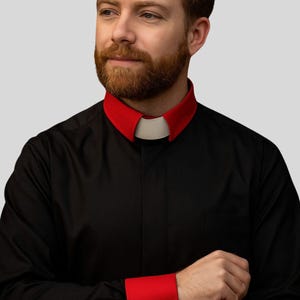 May include: Black dress shirt with a red collar and cuffs. The shirt has a white collar insert and black cuff links. The sleeves are long and the shirt has a pocket on the left side.