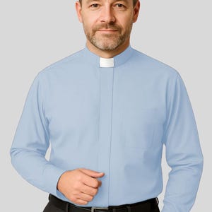 May include: A light blue long-sleeve shirt with a white clerical collar. The shirt has a chest pocket and is paired with black pants and a black belt. The man in the image is wearing a light blue shirt.