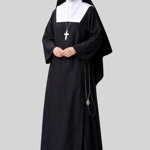 Puede incluir: Un hábito negro que consiste en un vestido largo de manga larga, una toca blanca y un velo negro. Un colgante de cruz plateada cuelga de una cadena alrededor del cuello y un rosario plateado con un medallón cuelga de la cintura.