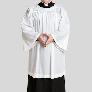 Op de afbeelding: Een witte albe met een zwarte kraag en een zwarte rok. De albe heeft wijde mouwen en een geplooide halslijn. De persoon draagt een zwarte geestelijke kraag. De outfit is een religieus gewaad.