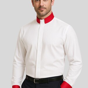 May include: White dress shirt with a mandarin collar and red accents on the collar and cuffs. The shirt has long sleeves and a button-down front. The model is wearing a black belt and dark blue pants.