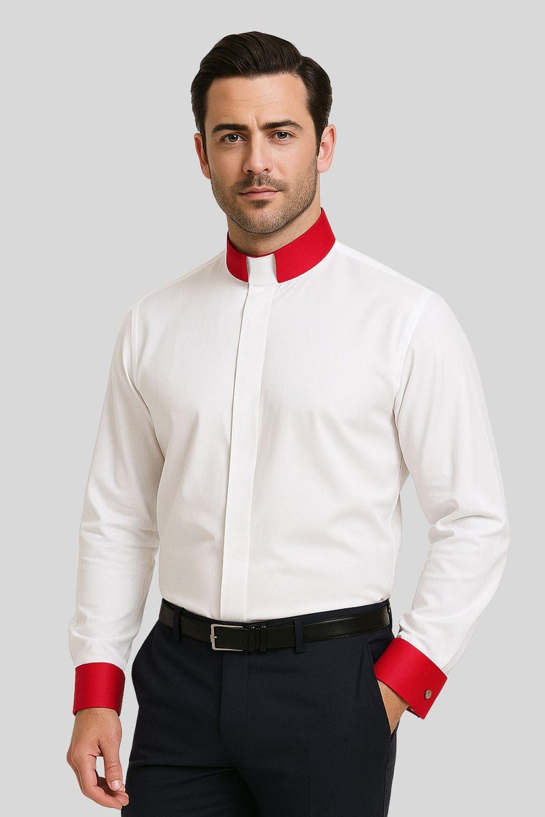 May include: White dress shirt with a mandarin collar and red accents on the collar and cuffs. The shirt has long sleeves and a button-down front. The model is wearing a black belt and dark blue pants.