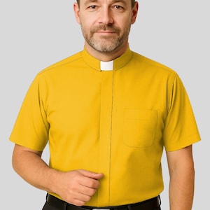 May include: A short-sleeved, mustard yellow shirt with a white clerical collar and a chest pocket. The shirt is buttoned down the front and is paired with black pants and a black belt.