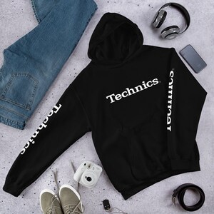 Könnte beinhalten: Schwarzer Kapuzenpullover mit weißem Text auf der Vorderseite, der "Technics" lautet, und weißem Text auf den Ärmeln, der "Technics" lautet.