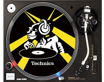 May include: A black turntable with a yellow and black slipmat featuring a cartoon illustration of a DJ wearing headphones. The slipmat has the text "Technics" printed on it.