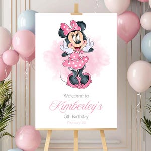Könnte beinhalten: Ein weißes Schild auf einer Staffelei zeigt eine Minnie Mouse-Illustration in einem rosa gepunkteten Kleid und einer Schleife. Auf dem Schild steht "Willkommen zu Kimberleys 5. Geburtstag 22. Februar" in rosa Schrift. Rosa und blaue Ballons umgeben das Schild.