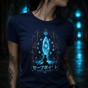 Könnte beinhalten: Marineblaues T-Shirt mit einem Fantasy-Motiv. Das Design zeigt einen leuchtenden blauen Kristall, eine Figur und eine gotische Struktur. Japanischer Text lautet "Save Point". Detaillierte Illustration.