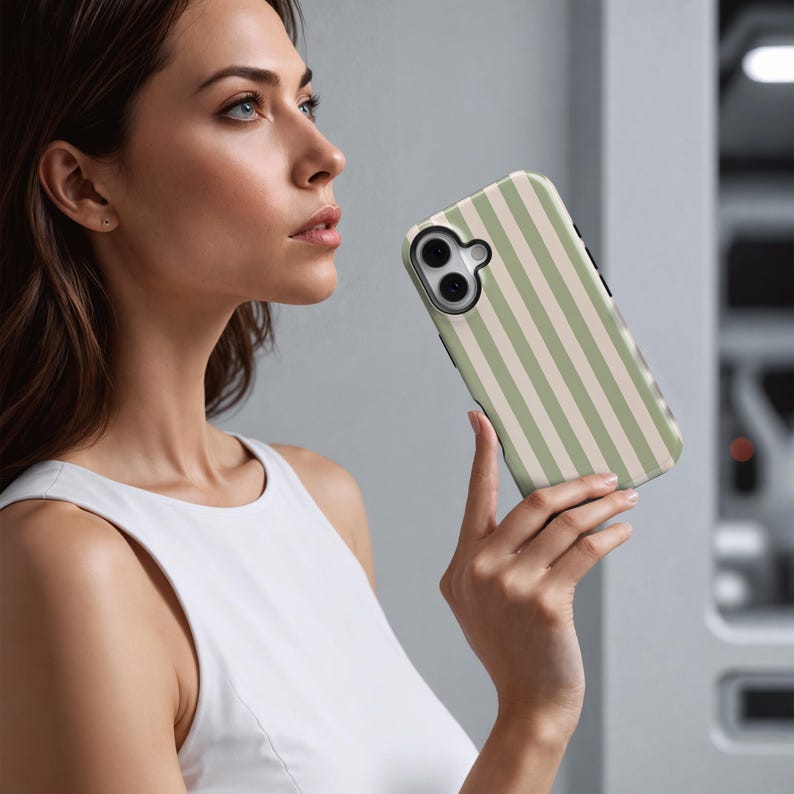 May include: A smartphone case with a vertical striped pattern in light green and beige. The case has a camera cutout and a black border. The phone case is held in a person's hand.
