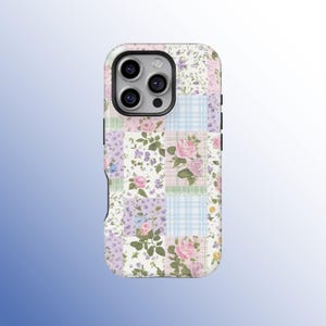 May include: A phone case with a patchwork design featuring floral patterns and pastel colours. The case has a mix of pink roses, purple flowers, and blue gingham squares. The case has a camera cutout and buttons.
