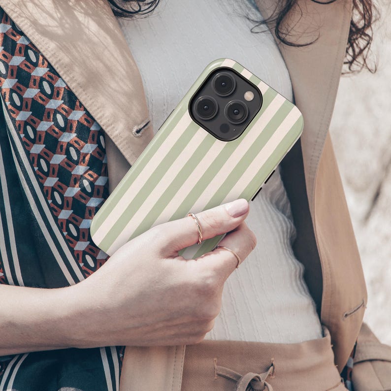 May include: A smartphone case with a vertical striped pattern in light green and off-white. The case is held in a person's hand, showcasing the design and the phone's camera array. The case is a protective accessory for a mobile phone.