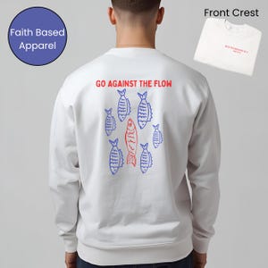 May include: White sweatshirt featuring the phrase "GO AGAINST THE FLOW" in red, with a fish graphic in red and blue. A small white t-shirt with red text is visible. The sweatshirt has a "Faith Based Apparel" logo.