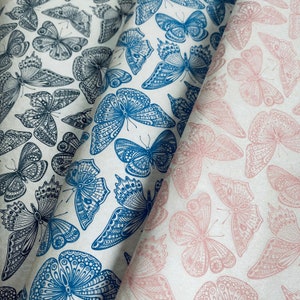 Puede incluir: Dos hojas de papel de regalo con un patrón de mariposa. Una hoja es azul y blanca con un diseño de mariposa detallado. La otra hoja es blanca con un diseño de mariposa rosa.