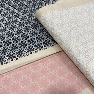 Puede incluir: Tres hojas de papel de regalo con un patrón floral. La hoja superior es negra con flores blancas, la hoja del medio es beige con flores blancas y la hoja inferior es rosa con flores blancas.