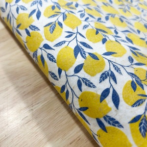 Può includere: Un rotolo di carta decorativa con un motivo ripetuto di limoni gialli e foglie blu su sfondo bianco. I limoni sono di un giallo brillante e le foglie di un blu intenso. La carta ha un aspetto strutturato.