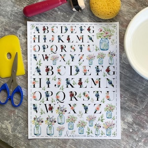 May include: A sheet of floral alphabet letters with watercolor mason jars. The letters are black with floral accents in pink, blue, and burgundy. The sheet includes the text "elan.decals.com".