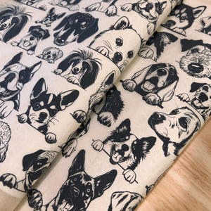 May include: Off-white wrapping paper with a repeating pattern of various dog breeds in black ink. The dogs are depicted in a cartoon style, with some peeking over the edge of the paper. The paper is folded, showing the pattern at different angles.