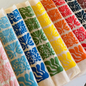 Puede incluir: Un conjunto de diez hojas de papel de regalo de colores con un patrón repetido de diseños florales estilizados. Los colores son rosa, azul, verde, amarillo, naranja y rojo.