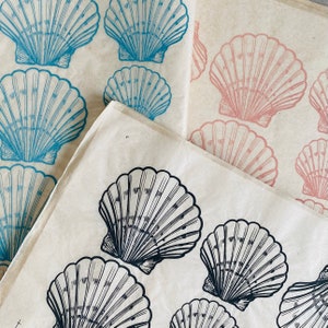 May include: A sheet of paper with a pattern of seashells printed on it. The seashells are in shades of blue, pink, and black. The paper is folded in half, and the pattern is visible on both sides.