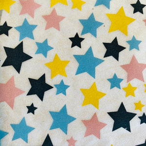 Op de afbeelding: Een witte achtergrond met een patroon van sterren in verschillende kleuren, waaronder roze, geel, blauw en zwart.