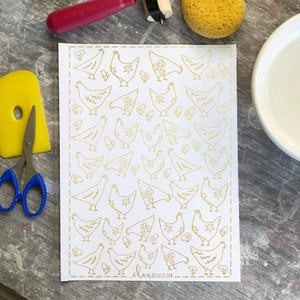 May include: A sheet of gold foil stickers featuring a repeating pattern of chickens and chicks. The stickers are on a white background and have a delicate, hand-drawn style. The sheet is labeled "elan DECALS.COM".