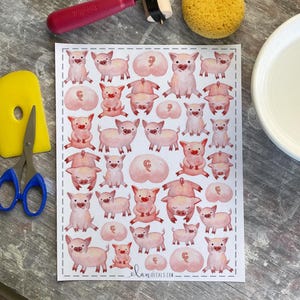 May include: Sheet of watercolor pig stickers in various poses, including standing, sitting, and lying down. The stickers are pink with red accents and feature the text "elan decals.com" at the bottom.