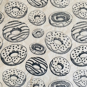 May include: A brown paper bag with a repeating pattern of black and white donuts. The donuts have different toppings, including sprinkles, chocolate, and stripes.