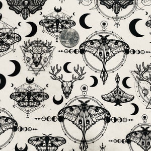 Op de afbeelding: Zwart-witte stof met een herhalend patroon van motten, hertenschedels, halve manen en geometrische vormen. De stof heeft een vintage uitstraling.
