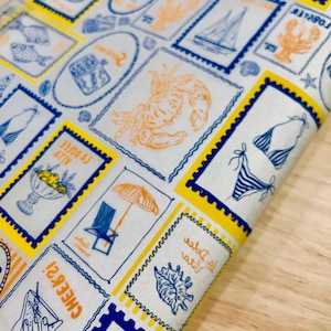 Puede incluir: Tela blanca con un patrón repetido de diseños de sellos postales azules y naranjas con temática playera. Los sellos presentan imágenes de una langosta, un velero, un bikini y una sombrilla. Los sellos están delineados en azul y amarillo.