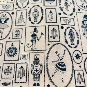 May include: Cream-colored fabric with a repeating pattern of navy blue Christmas-themed illustrations. The design includes nutcrackers, ballerinas, Christmas trees, bells, ornaments, and a mouse in a crown. The illustrations are framed in decorative borders.