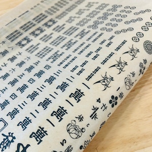 May include: A sheet of brown paper with black ink designs. The designs include various symbols, birds, and flowers. The paper is folded in half and the designs are visible on both sides.