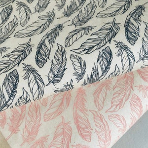 Puede incluir: Dos hojas de papel de regalo con un patrón de plumas. Una hoja tiene plumas negras sobre un fondo blanco, y la otra hoja tiene plumas rosas sobre un fondo blanco.