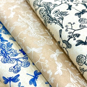 Puede incluir: Tres rollos de papel de regalo con diferentes patrones. El rollo superior tiene un patrón floral blanco y negro con libélulas. El rollo del medio tiene un patrón floral blanco con libélulas sobre un fondo marrón. El rollo inferior tiene un patrón floral azul con libélulas sobre un fondo blanco.