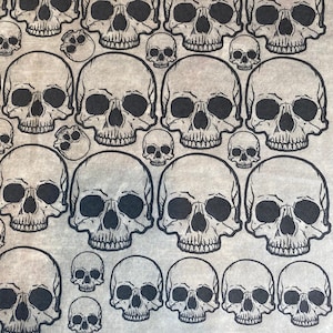 May include: A seamless pattern of black and white skull illustrations on a beige background. The skulls are of varying sizes and are arranged in a repeating pattern.