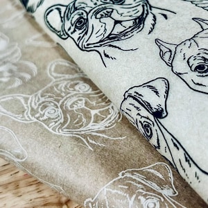Puede incluir: Una hoja de papel de envolver marrón con un patrón repetido de ilustraciones en blanco y negro de Bulldogs franceses. El papel está doblado sobre sí mismo, mostrando el patrón en ambos lados.