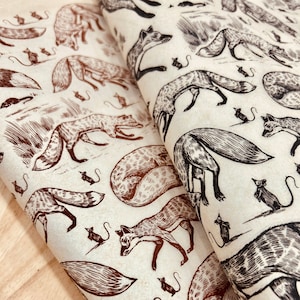 Puede incluir: Dos hojas de tela con un patrón repetido de zorros y ratones en tinta marrón y negra. Los zorros se representan en varias poses, algunos corriendo, otros acurrucados. El fondo es de color crema.