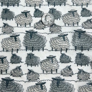 May include: White fabric with a repeating pattern of black and gray sheep. The sheep are stylized and have a simple design. The fabric is textured and has a slightly rough feel.