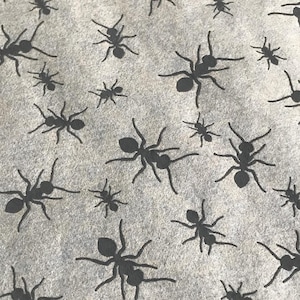 May include: A close-up of a gray fabric with a repeating pattern of black ants. The ants are all facing the same direction and are arranged in a staggered pattern.