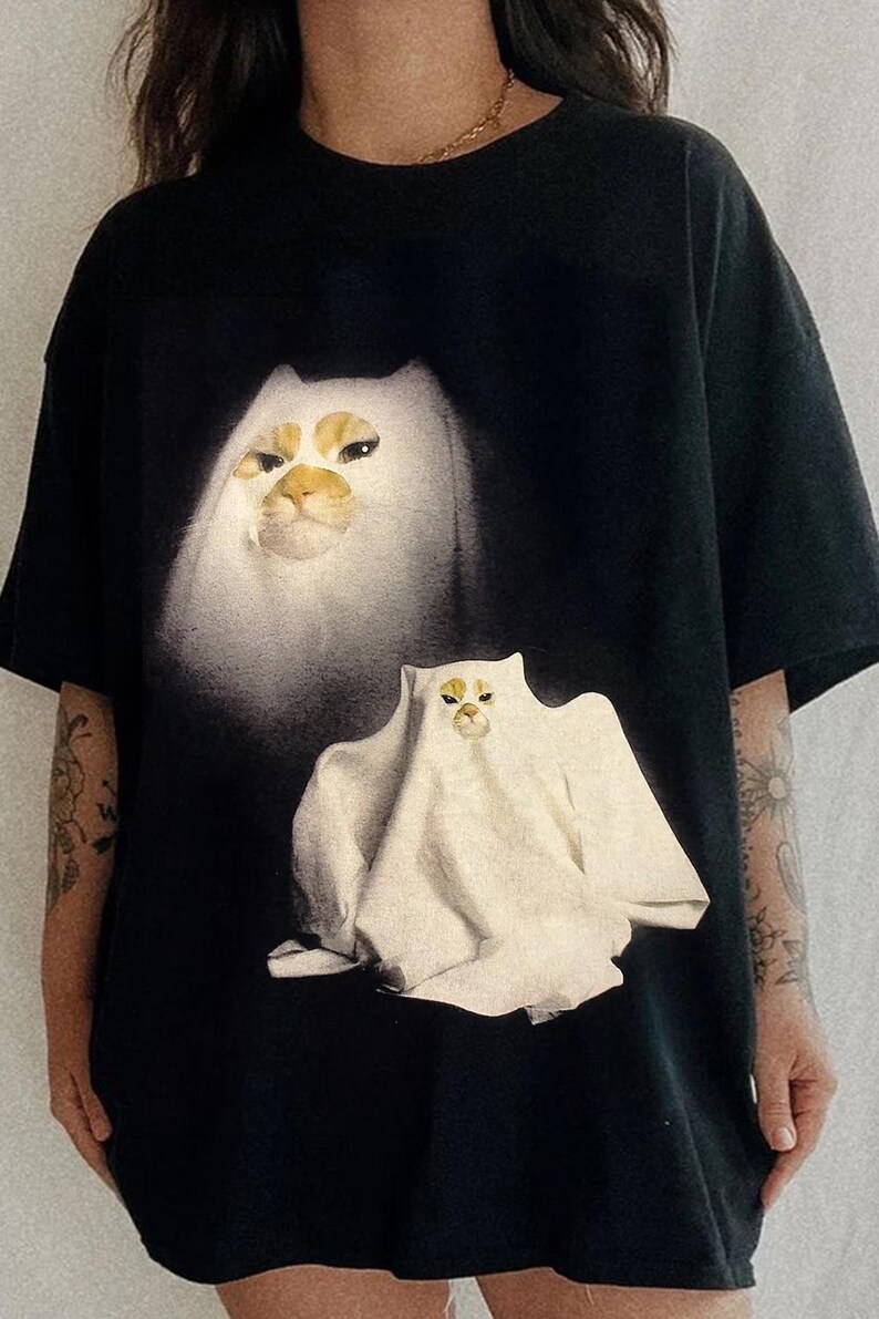 Pu&ograve; includere: T-shirt nero con un disegno di gatto bianco dall'aspetto spettrale. Il gatto ha segni facciali gialli e marroni. Il disegno &egrave; stampato sul davanti. La maglietta ha maniche corte e girocollo.