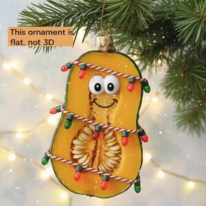 May include: A whimsical Christmas ornament shaped like a butternut squash, decorated with a string of colorful lights. The squash has a smiling face and the text "This ornament is flat. not 3D".