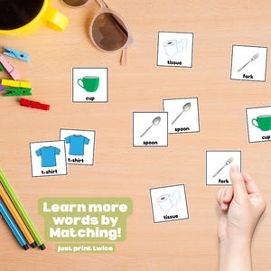 May include: Educational matching game with illustrated cards featuring a green cup, blue t-shirts, spoons, forks, and tissue. The text "Learn more words by Matching!" is visible. Other items include pens, a phone, and sunglasses.
