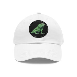 May include: White baseball cap with a circular patch displaying a green iguana illustration. The iguana is depicted in shades of green and black, set against a black background with a white stitched border. The cap has a curved peak.