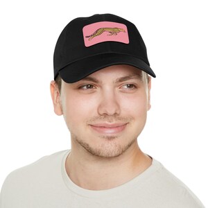 Peut inclure: Casquette de baseball noire avec un patch rectangulaire rose représentant un guépard jaune et noir. La casquette est faite d'une matière souple et possède une visière incurvée. Un accessoire élégant pour un usage décontracté.