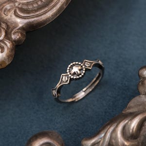 Op de afbeelding: Een zilveren ring met een sterontwerp in het midden, omringd door een cirkel van kralen en geometrische vormen. De ring staat tegen een donkerblauwe achtergrond, met een decoratief zilveren dienblad op de voorgrond.