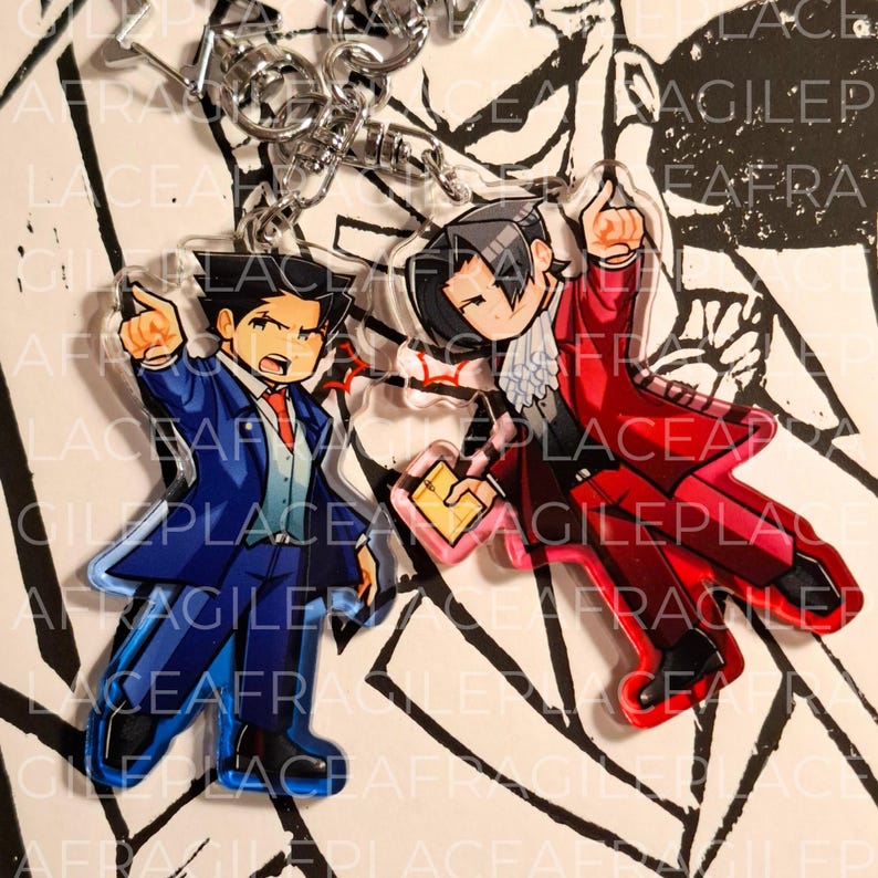 May include: Two acrylic keychains featuring chibi-style characters in suits. One character wears a blue suit and points forward, while the other wears a red suit with a white cravat, holds a yellow folder, and points upward. Both have silver clasps.