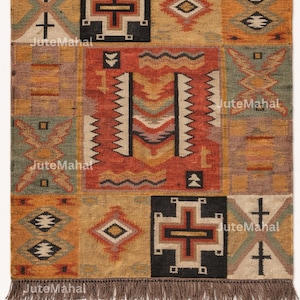 May include: A rectangular jute rug with a patchwork design. The rug features geometric patterns in shades of orange, brown, yellow, and green. The text "JuteMahal" is printed on the rug. The rug has a fringed edge.