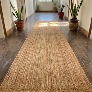 May include: A long, rectangular runner rug crafted from natural, light brown woven fibers. The rug features a consistent, braided texture throughout its entire length, creating a uniform surface that extends from the foreground into the distance.