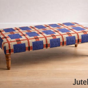 May include: A rectangular ottoman with a blue, red, and beige plaid pattern. The upholstered top sits on four wooden legs. The ottoman is a decorative furniture piece.